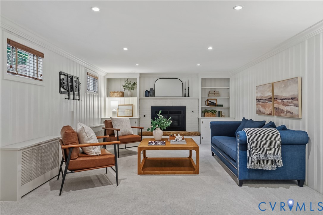 Vertical paneled walls, wood-burning fireplace with white brick surround, built-in shelving, recessed lighting, and wall-to-wall carpeting