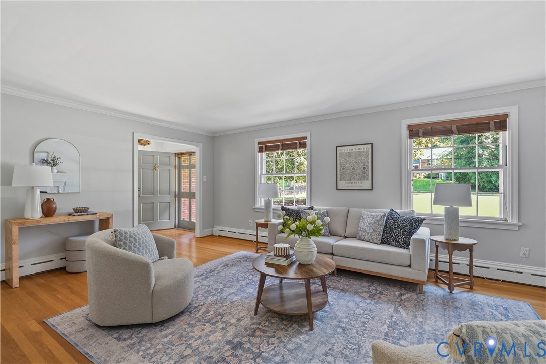 Living area featuring wood-finish flooring, multi-pane windows with trim casing, crown molding, and a paneled entry door