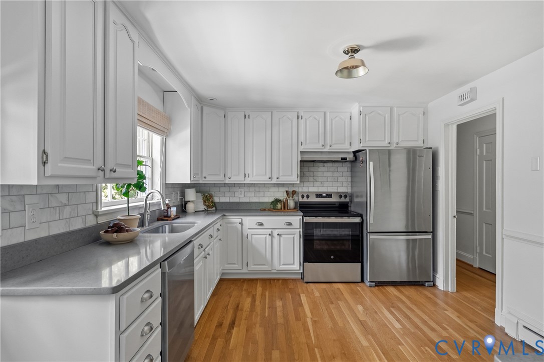 Kitchen featuring white cabinetry, solid-surface countertops, subway tile backsplash, stainless steel appliances, and wood-finish flooring