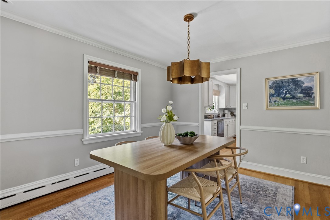 Dining area featuring hardwood flooring, chair rail molding, multi-pane window, and a metallic tiered pendant light fixture
