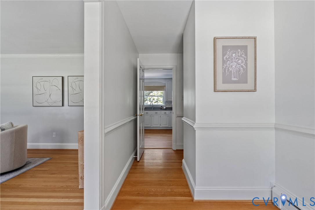 Interior hallway featuring wood-finish flooring, white walls, and traditional chair rail molding