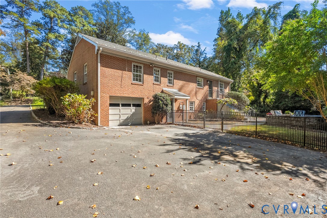 Two-story brick exterior featuring an attached one-car garage, asphalt driveway, metal fencing, and multi-pane windows