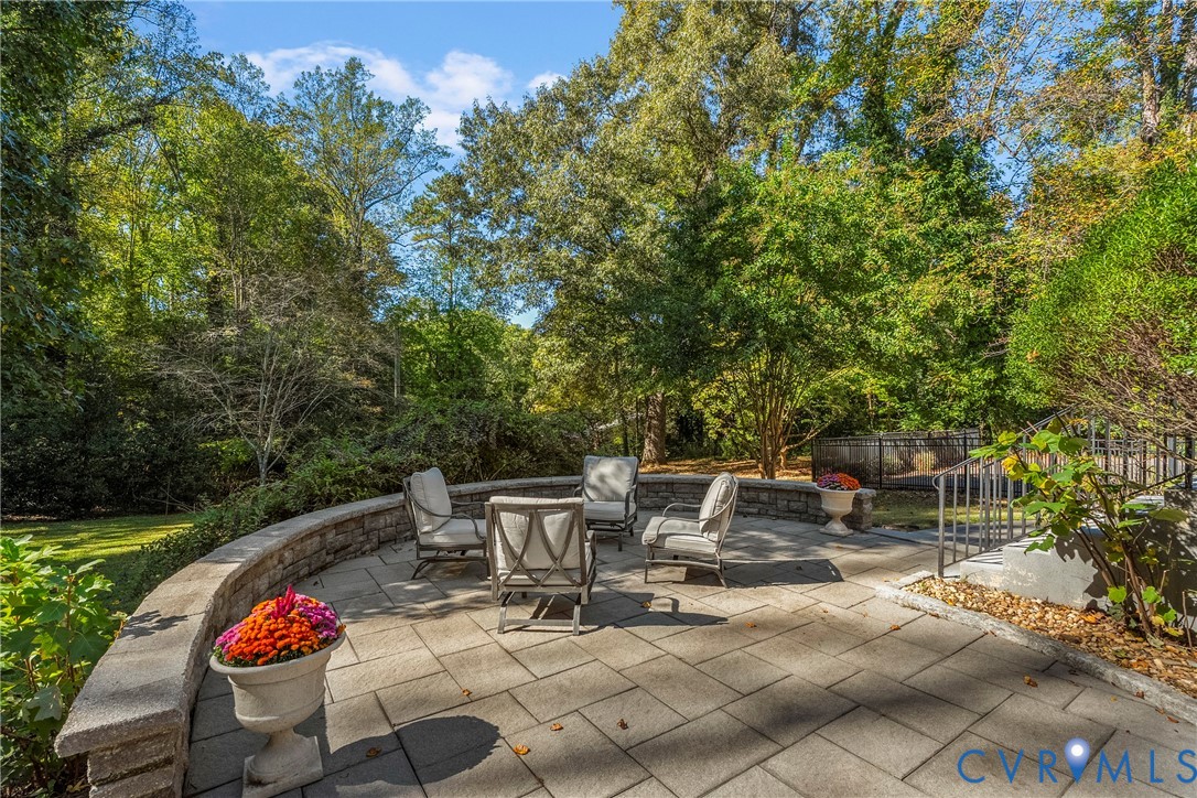 Stone paver patio featuring a curved retaining wall, built-in stone masonry, and mature tree-lined surroundings