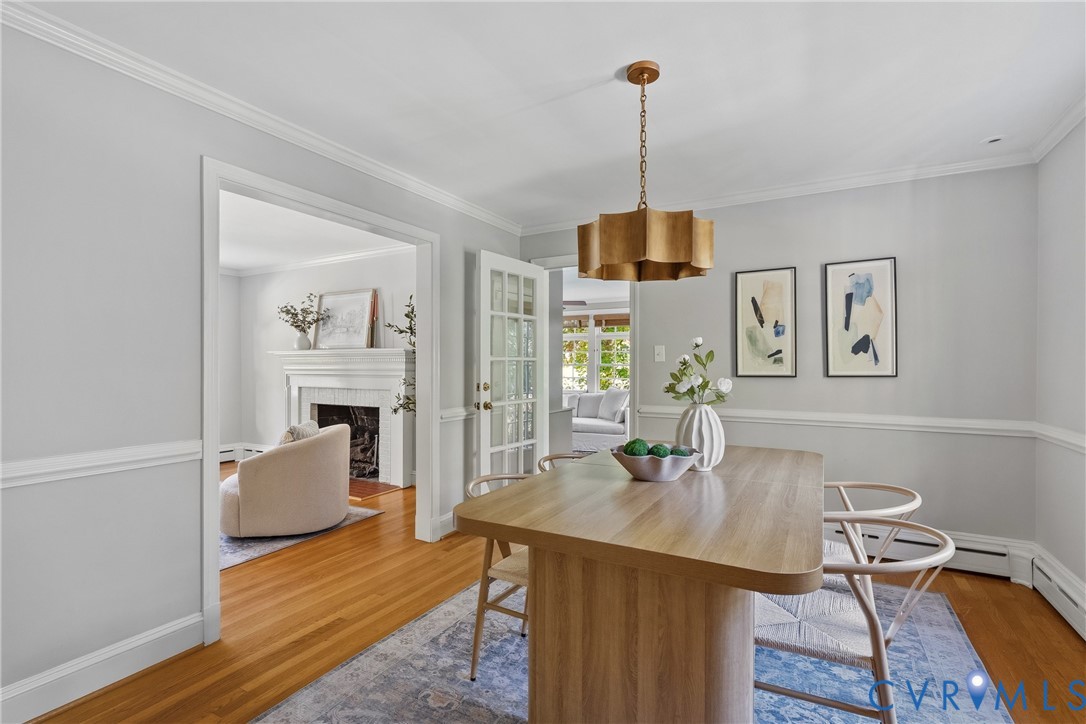 Dining area featuring hardwood flooring, crown molding, chair rail trim, a multi-pane glass door, and a metallic tiered chandelier
