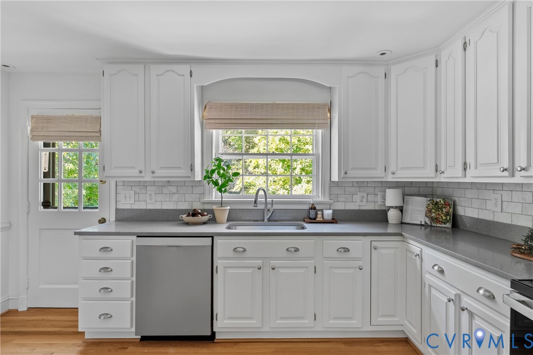 Kitchen featuring white recessed-panel cabinetry, solid-surface countertops, a white subway-tile backsplash, stainless steel dishwasher, and hardwood flooring