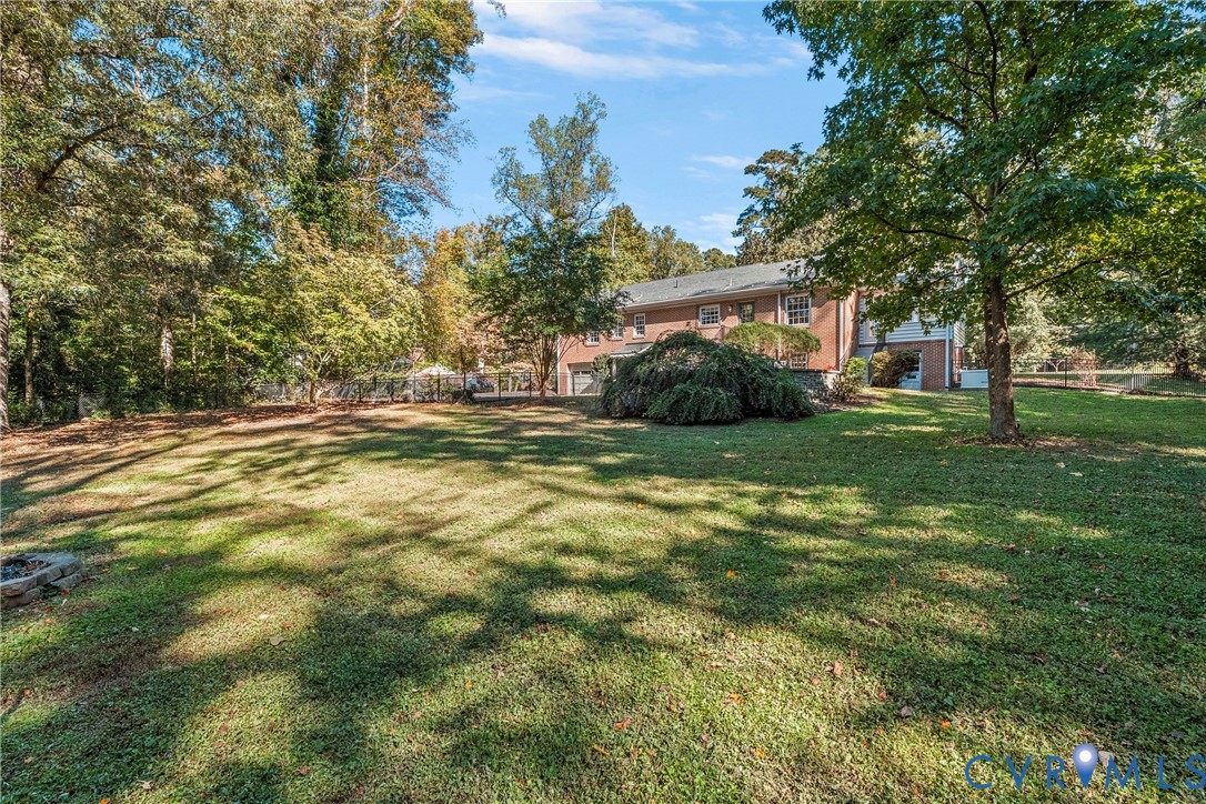 Expansive backyard featuring a manicured lawn, established shade trees, perimeter fencing, and a brick exterior residence