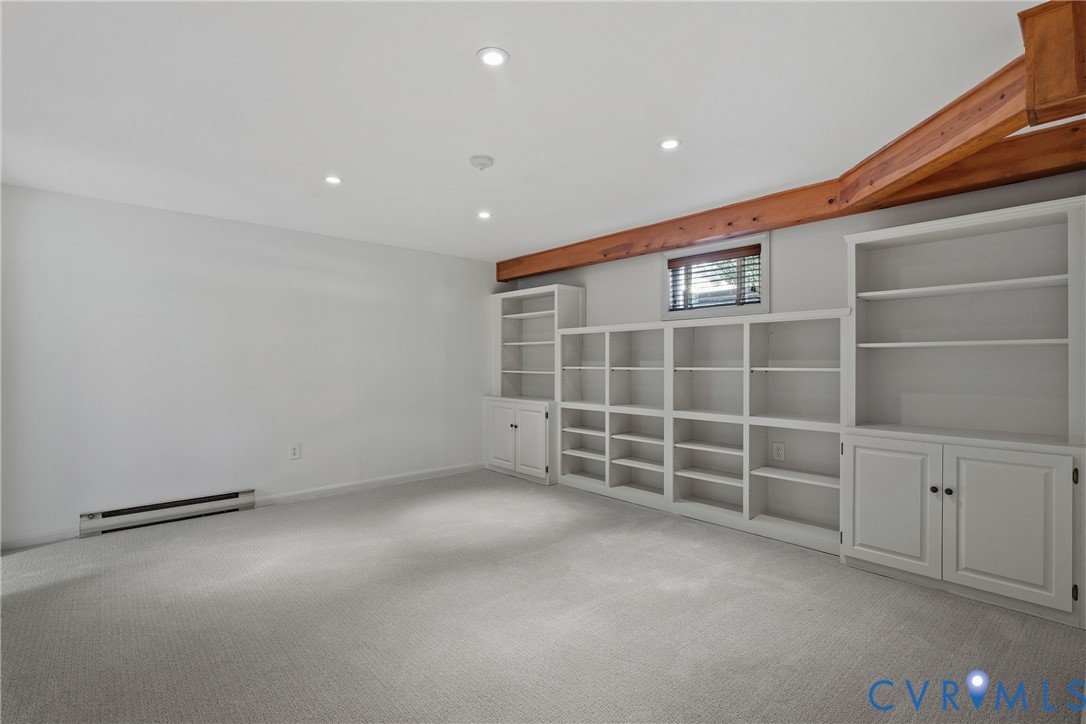 Room featuring exposed natural wood ceiling beams, expansive wall-to-wall built-in shelving, and recessed lighting