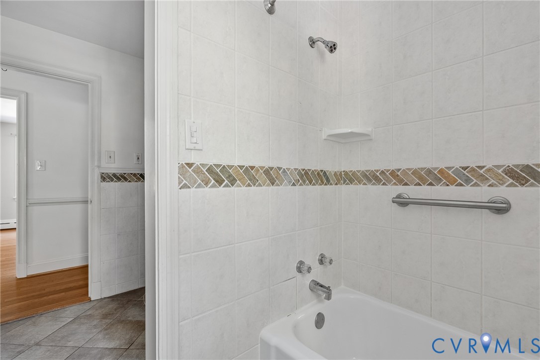 Bathtub with wall-mounted shower head, built-in shelving, herringbone tile accent border, and metal safety rail