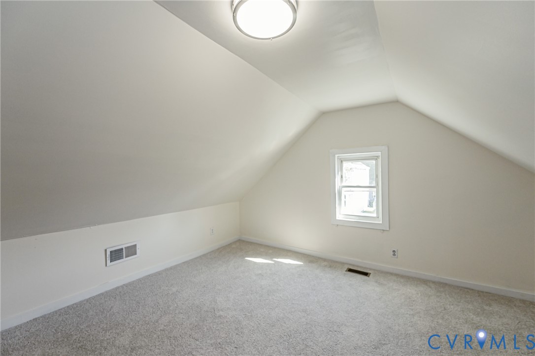 Finished room with neutral carpet flooring, vaulted ceilings, and a central overhead flush-mount light fixture