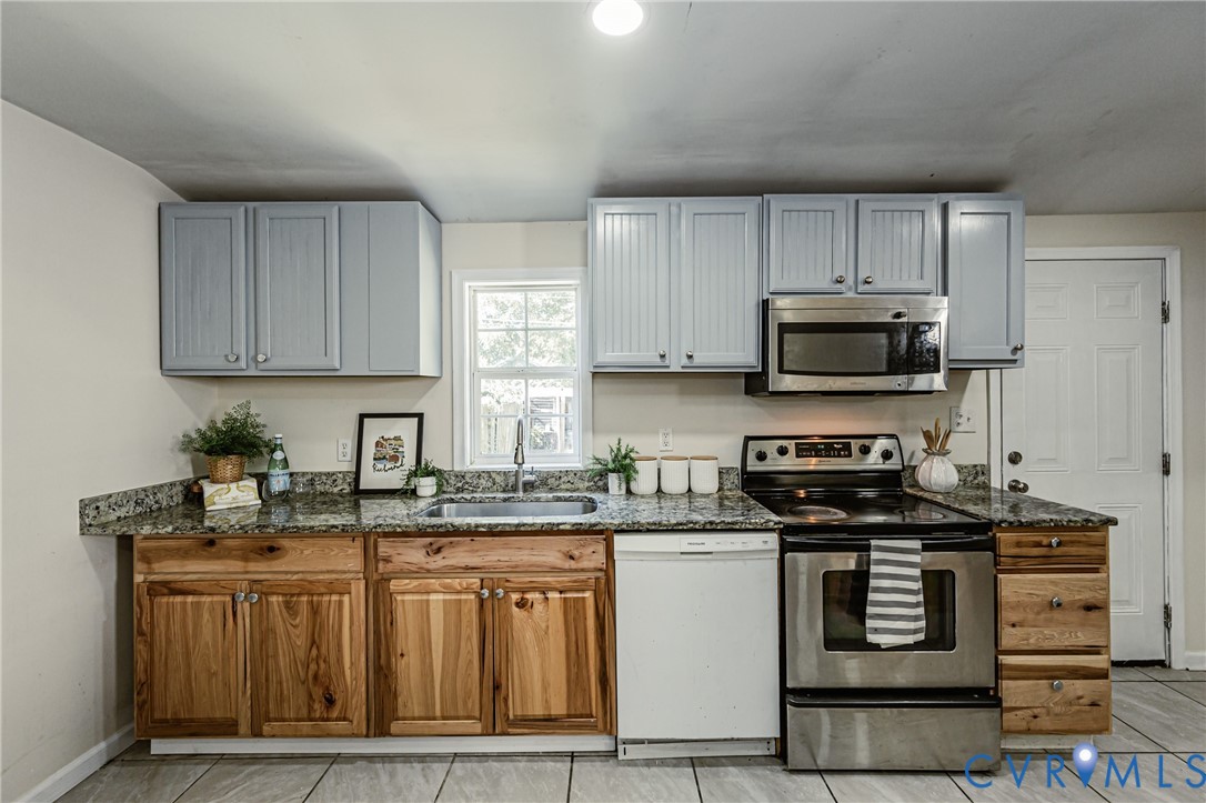 Kitchen featuring two-tone cabinetry with wood-finish lower cabinets and light-painted upper cabinets, stone-surfaced countertops, stainless steel appliances, and tile flooring