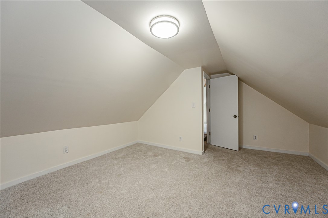 Finished interior space with vaulted ceilings, neutral wall tones, wall-to-wall carpeting, and a flush-mount circular ceiling light
