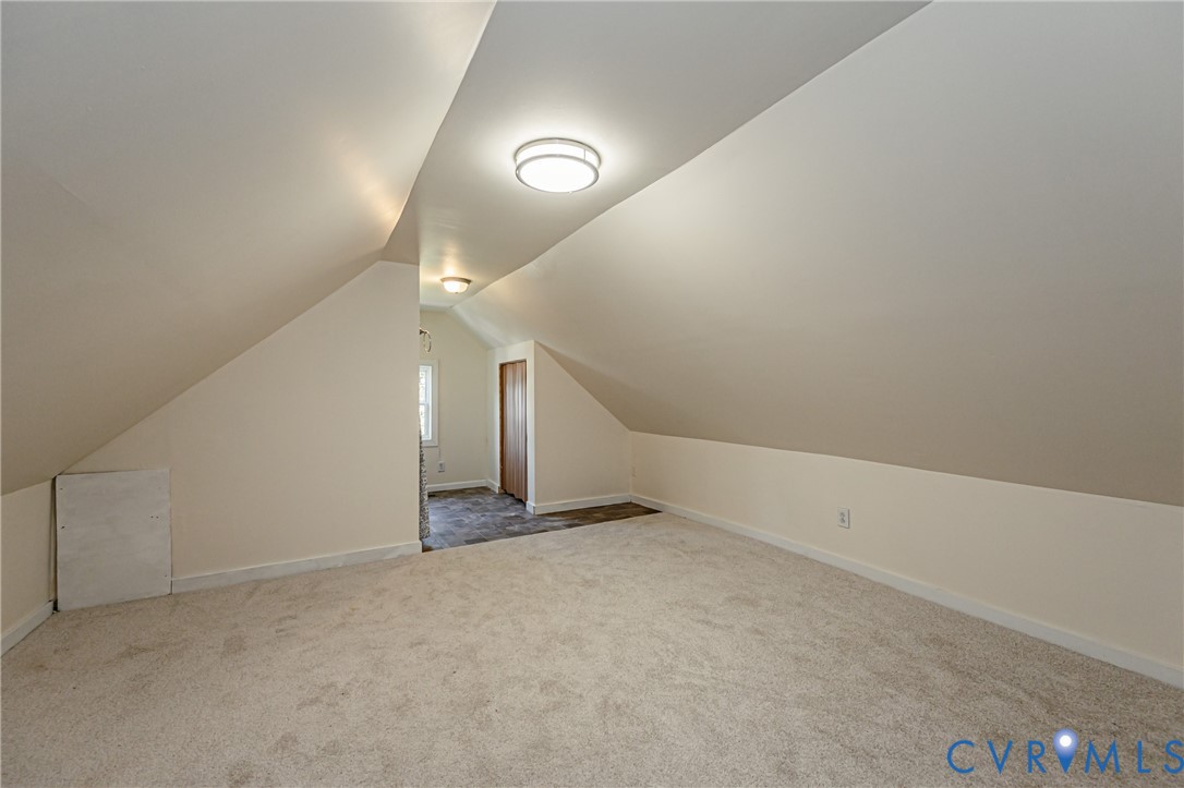 Finished attic space featuring vaulted ceilings, neutral wall-to-wall carpeting, dual flush-mount ceiling light fixtures, and a built-in closet
