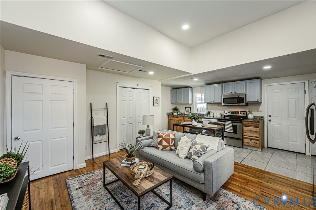Open-concept interior featuring vaulted ceilings, wood-finish flooring, recessed lighting, and kitchen cabinetry with a mix of neutral-toned upper and natural wood-tone lower finishes