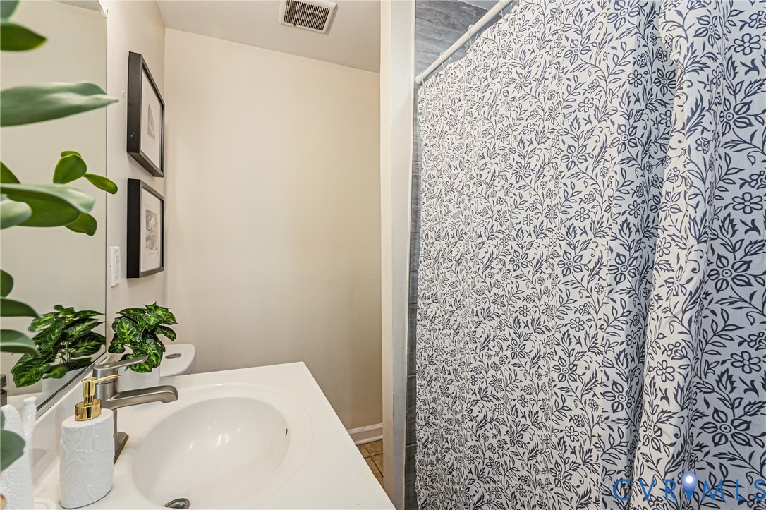 Bathroom featuring a white vanity with a single-basin sink, brushed metal faucet, large wall-mounted mirror, and a shower area with grey-toned wall tiling