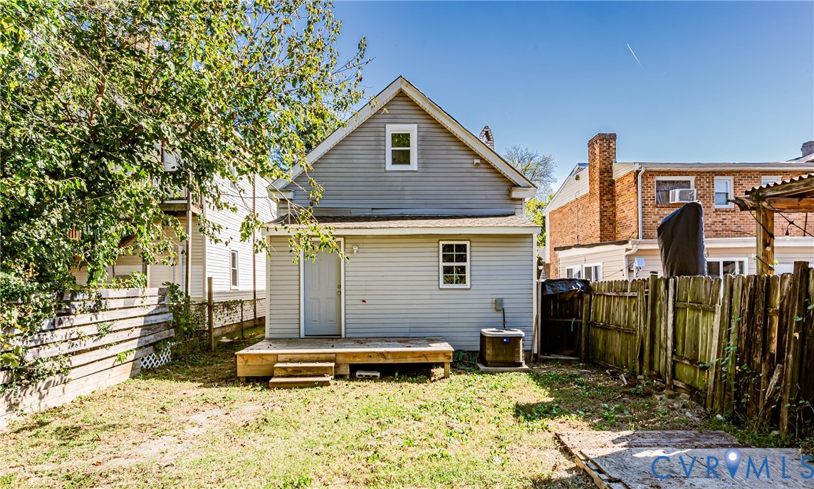 Rear exterior featuring light grey siding, a raised wood deck with steps, and a fenced backyard
