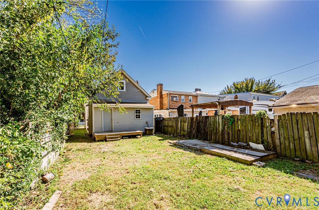 Backyard area featuring a wooden deck, wood privacy fencing, mature trees, and an open grass lawn