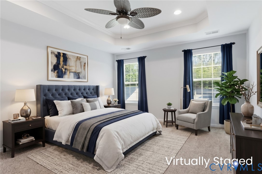 Light-filled primary bedroom with a tray ceiling, updated ceiling fan, and soft carpeting. [Photo has been digitally staged]