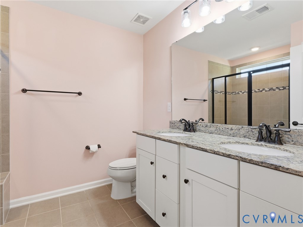 Primary ensuite bathroom featuring a double vanity, glass shower, and cabinet storage
