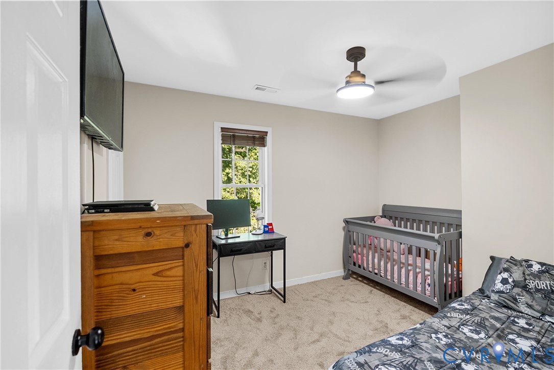 Neutral-toned bedroom featuring carpeted flooring, a multi-pane window with a woven shade, and a flush-mount ceiling fan with an integrated light fixture