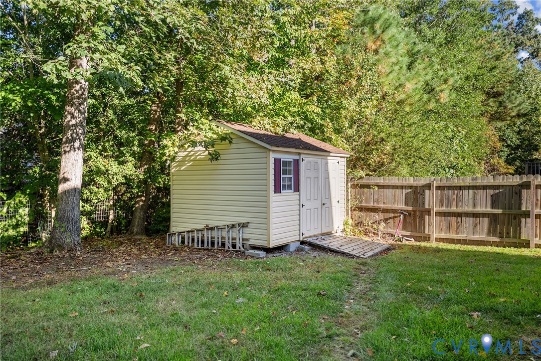 Backyard storage shed featuring vinyl siding, a single window, double-door entry with a ramp, and wood fencing