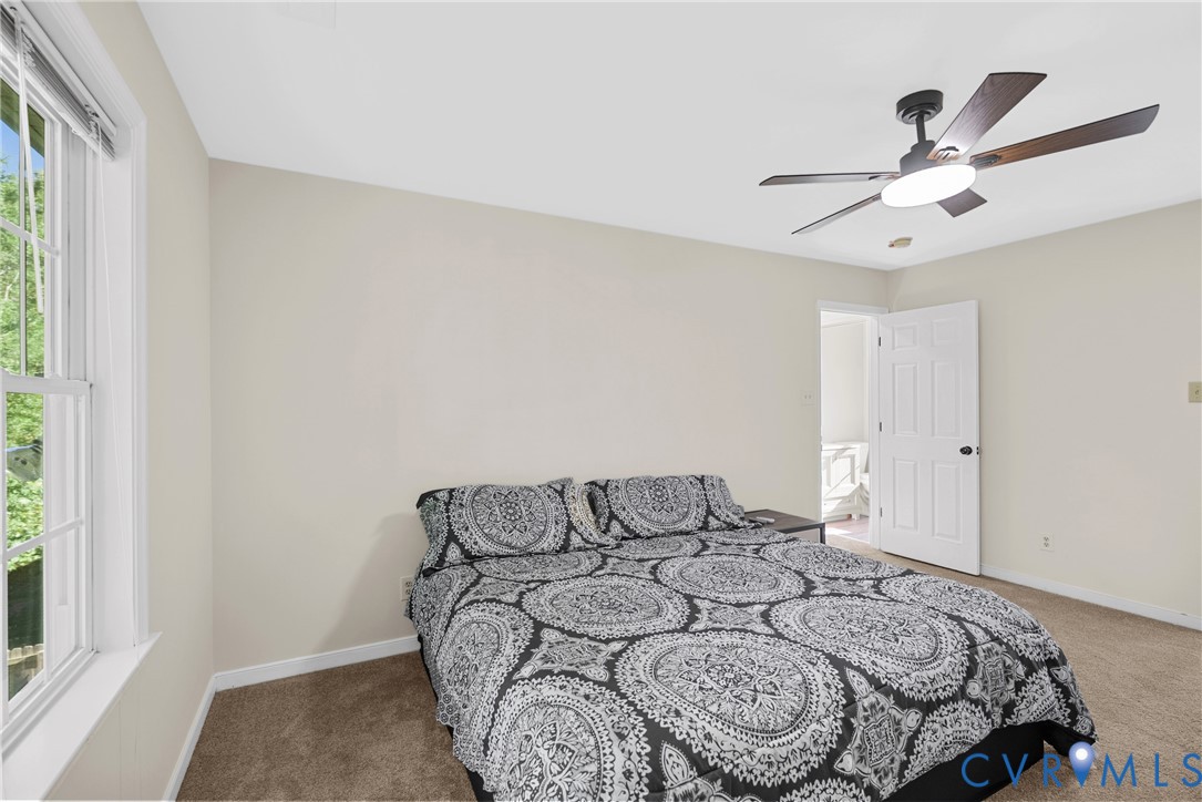 Neutral-toned walls, carpeted flooring, multi-pane window, and a ceiling-mounted light fixture with a fan
