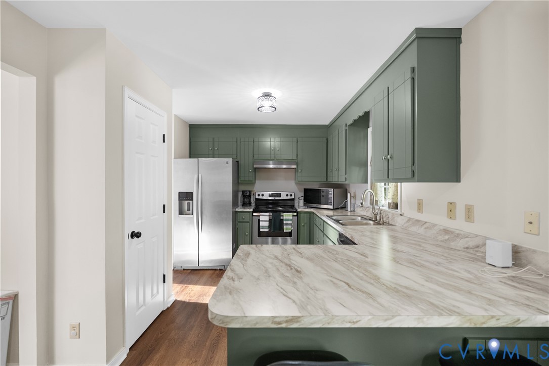 Kitchen featuring sage green cabinetry, stone-patterned laminate countertops, stainless steel appliances, wood-finish flooring, and a flush-mount ceiling light