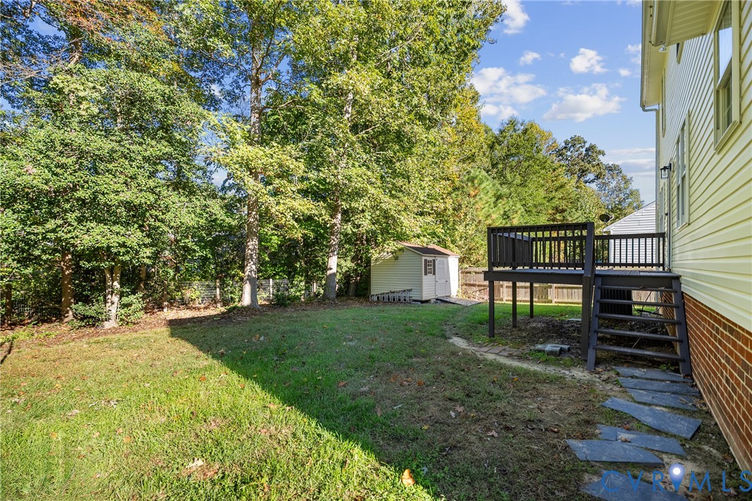 Rear exterior featuring a raised wood deck with stair access, stone paver pathway, detached storage structure, and tree-lined perimeter