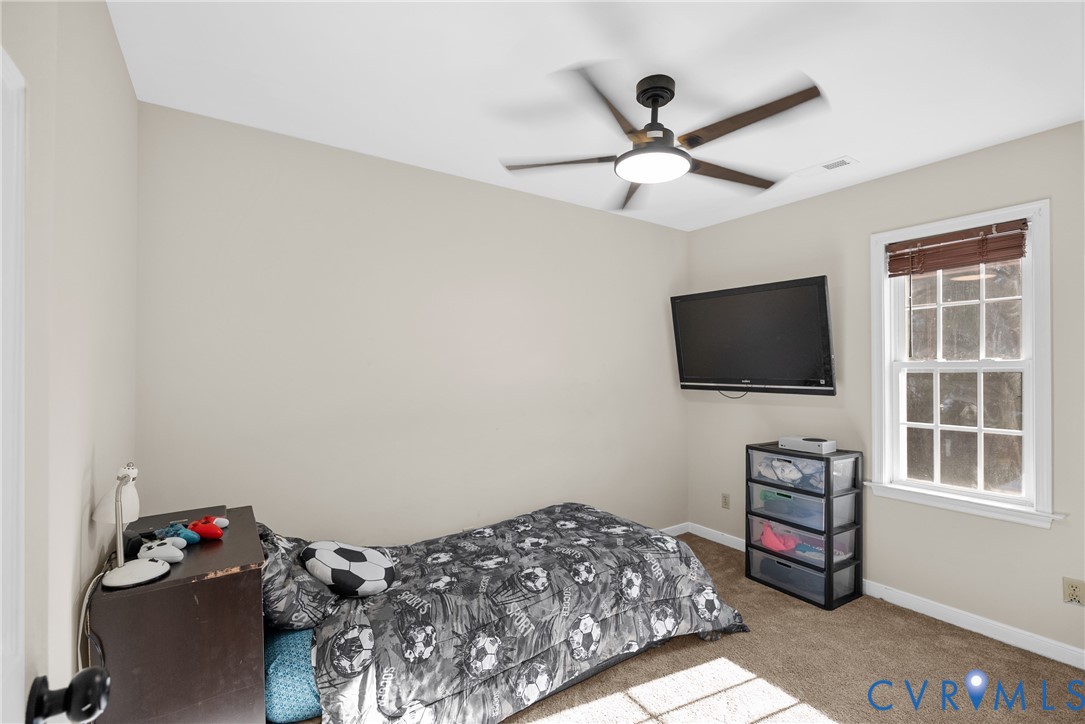 Neutral-toned interior room featuring wall-to-wall carpeting, a multi-pane window with wood-finish blinds, and a ceiling-mounted light fixture with a fan