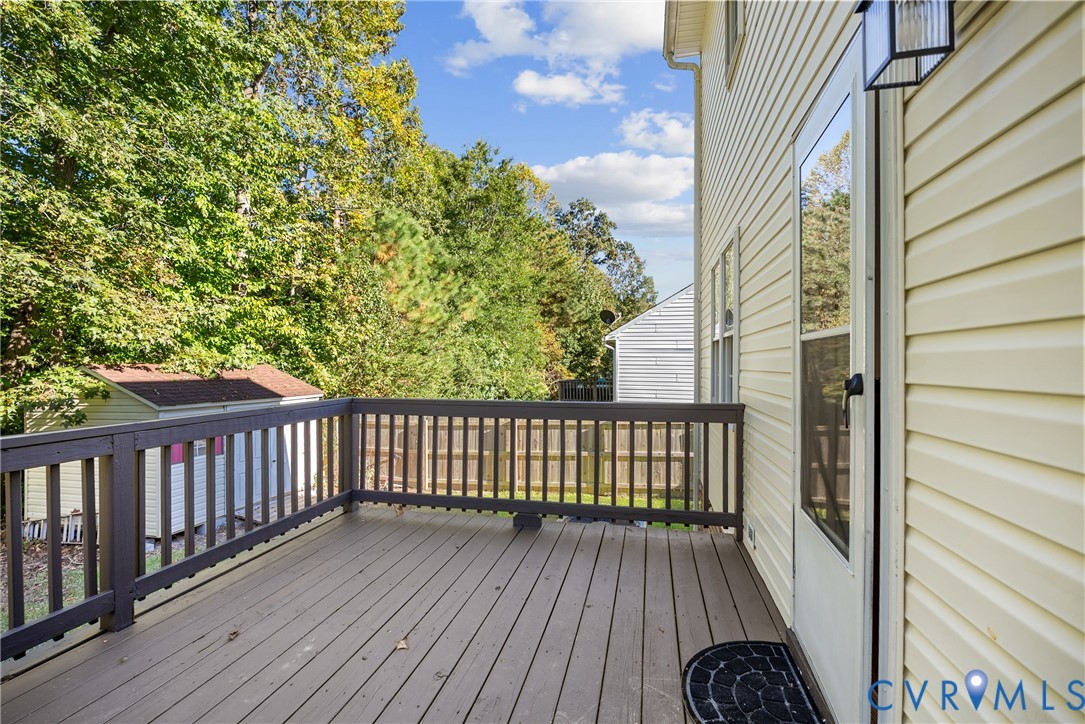 Raised deck with wood-finish decking and dark-toned railings, light-colored vinyl siding, and exterior wall-mounted lighting