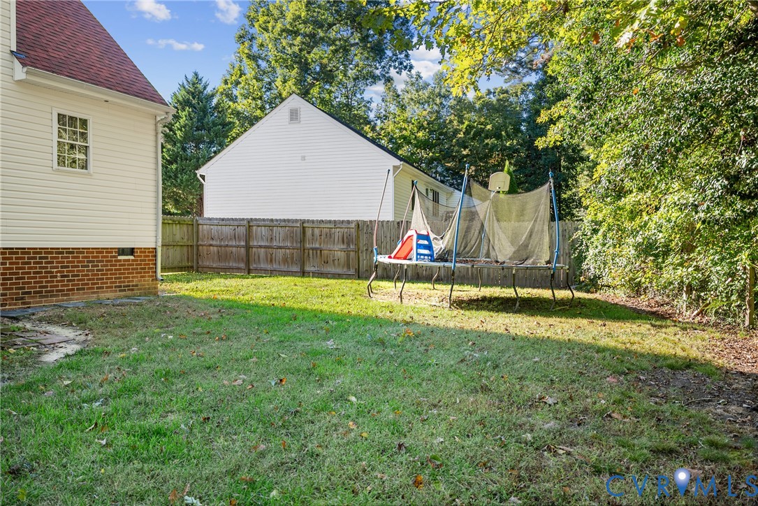 Rear exterior featuring light-colored siding, a brick foundation, and a fenced backyard with mature trees