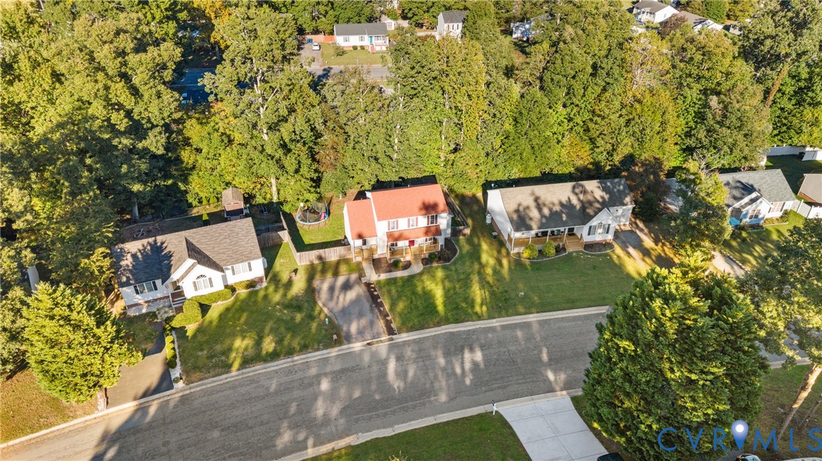 Aerial perspective of a multi-structure residential neighborhood featuring asphalt paved streets, concrete driveways, dense mature tree coverage, and managed lawns