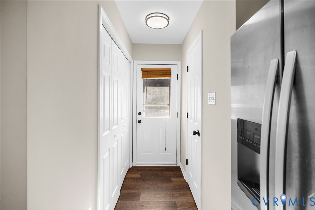 Hallway featuring wood-finish flooring, a white six-panel door with a glass insert, dual bifold closet doors, and a circular flush-mount ceiling light fixture Hallway featuring wood-finish flooring, a white six-panel door with a glass insert, dual bifold closet doors, and a circular flush-mount ceiling light fixture