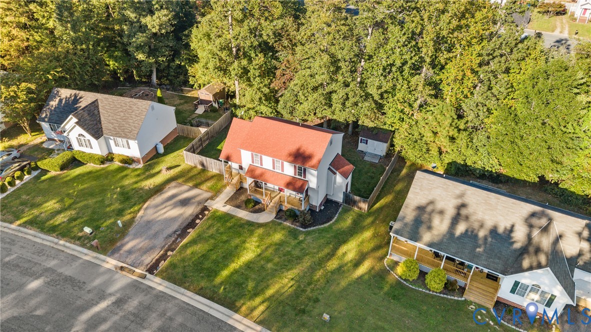 Two-story residential structure featuring a red metal roof, covered front entryway, asphalt driveway, and private fenced yard space