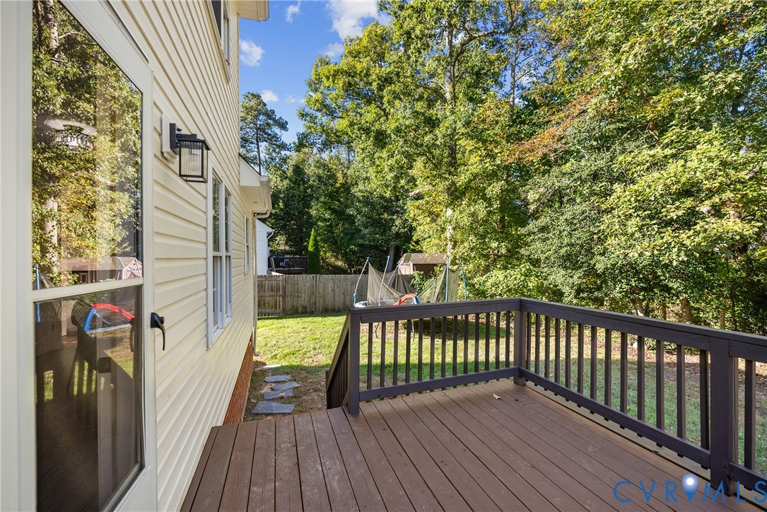 Exterior deck featuring dark wood-finish planking and dark-toned railings, light-colored vinyl siding, and wall-mounted outdoor lighting