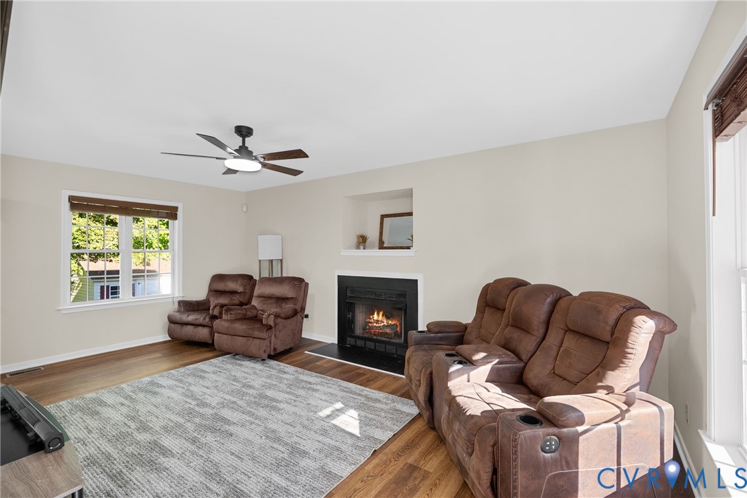 Wood-finish flooring, fireplace with a black surround, recessed wall niche, and ceiling fan with integrated lighting