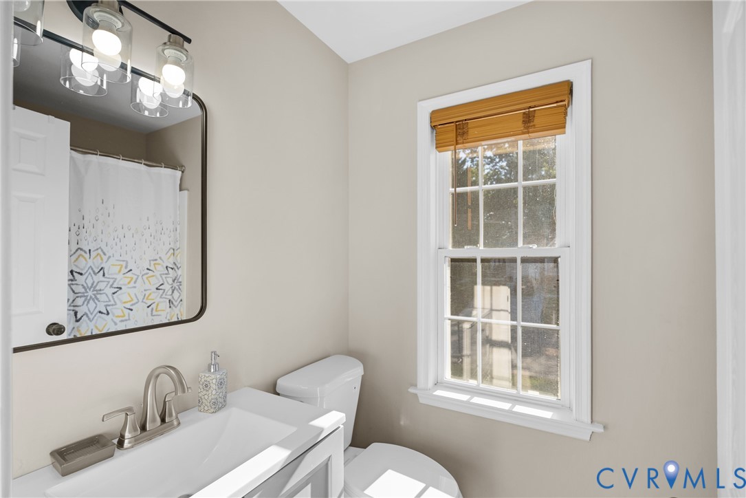Bathroom featuring a vanity with a white rectangular sink, brushed nickel faucet, wall-mounted mirror with rounded corners, three-light vanity fixture, and a multi-pane window