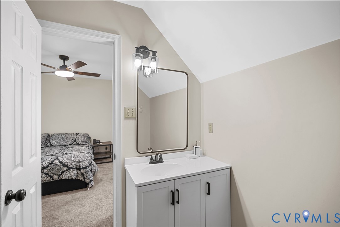 Vanity featuring light gray cabinetry, white countertop with integrated sink, matte black hardware, rectangular mirror with thin dark frame, and three-bulb vanity light fixture