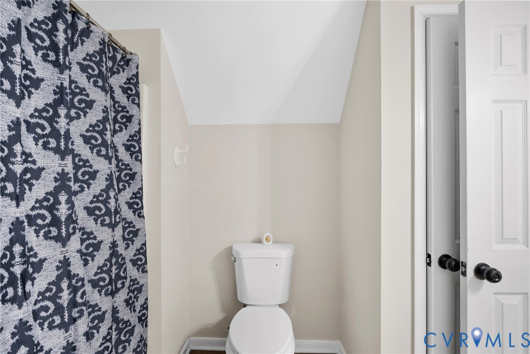 Bathroom featuring a white two-piece toilet, angled ceiling, and a paneled door with matte black hardware
