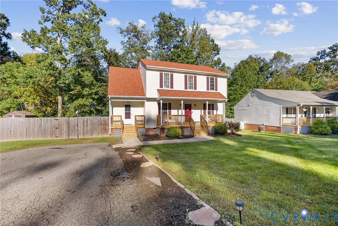 Two-story residence featuring light-colored siding, a metal-roofed covered front porch, decorative shutters, and a wood privacy fence Two-story residence featuring light-colored siding, a metal-roofed covered front porch, decorative shutters, and a wood privacy fence