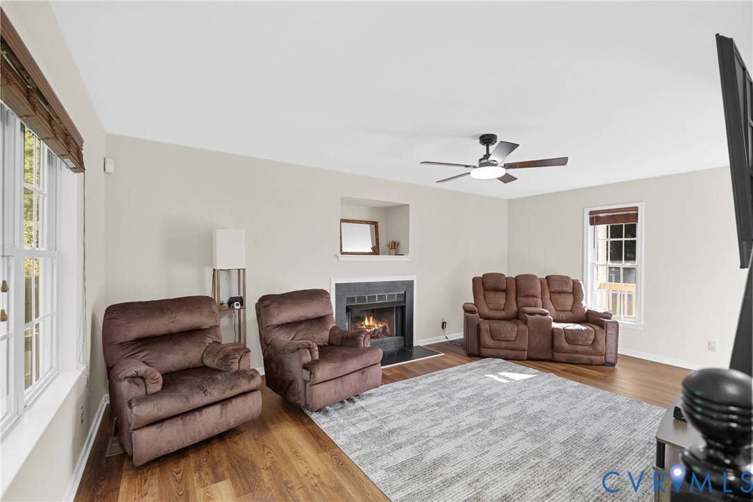 Living area featuring wood-finish flooring, a recessed fireplace with a dark surround, a built-in display niche, and a multi-blade ceiling fan with integrated lighting