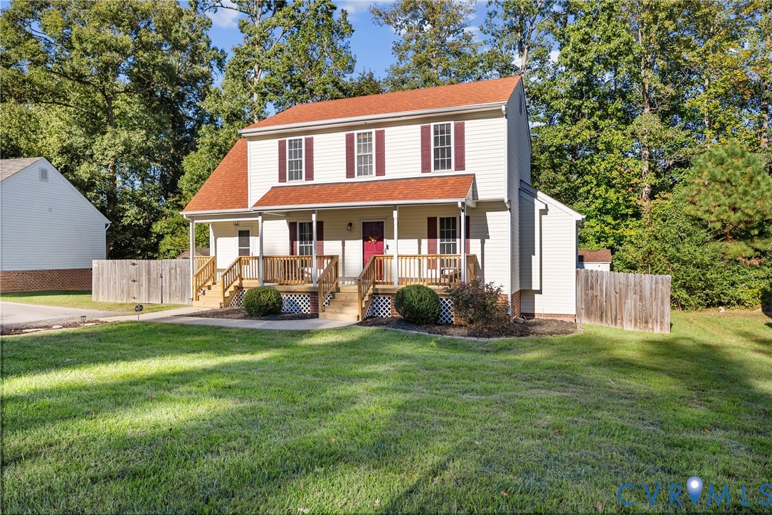 Two-story colonial residence featuring light-toned siding, dark shutters, a covered front porch, wooden deck railing, and a shingled roof