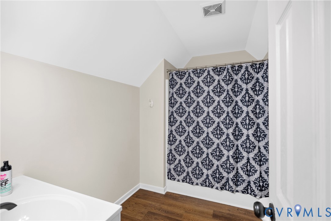 Bathroom featuring wood-finish flooring, vaulted ceilings, and a shower-tub combination