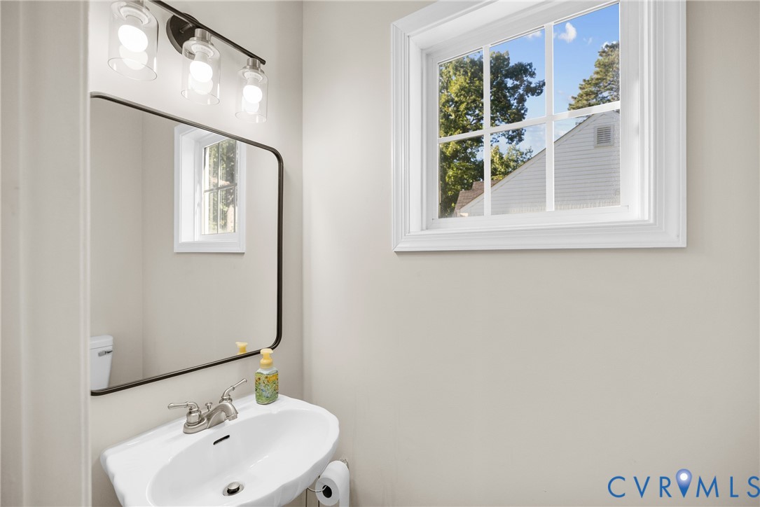 Wall-mounted white pedestal sink with polished chrome faucet, rectangular mirror with thin black frame, and three-light vanity fixture featuring clear glass shades and decorative bulbs Wall-mounted white pedestal sink with polished chrome faucet, rectangular mirror with thin black frame, and three-light vanity fixture featuring clear glass shades and decorative bulbs