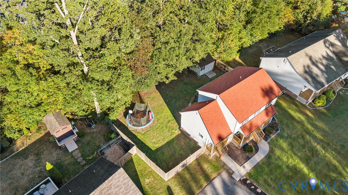Aerial perspective featuring a multi-level structure with a red roof, enclosed by wooden fencing, accompanied by a detached storage shed and mature trees