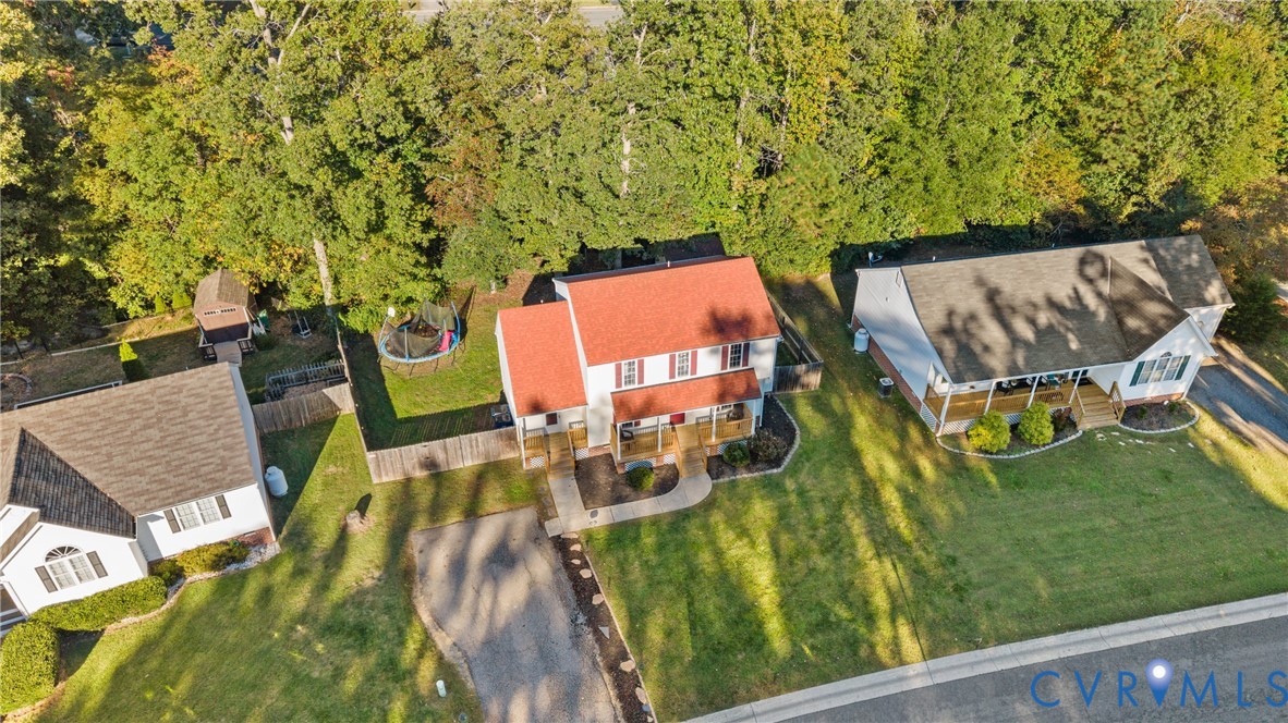 Two-story residence featuring a red shingled roof, front porch, concrete walkway, and a private rear yard with mature trees