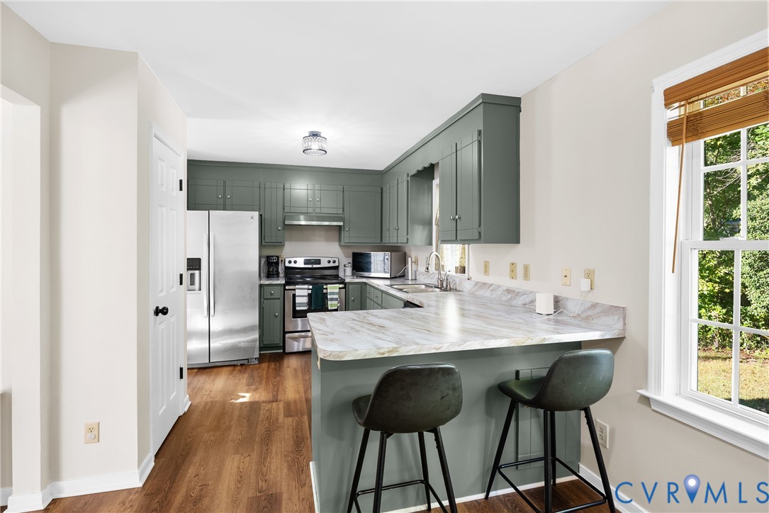 Kitchen featuring sage green cabinetry, stone-patterned countertops, stainless steel appliances, and wood-finish flooring Kitchen featuring sage green cabinetry, stone-patterned countertops, stainless steel appliances, and wood-finish flooring