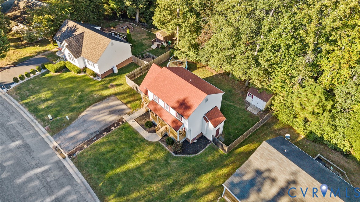 Aerial perspective of a two-story residence featuring a shingled roof, paved driveway, rear wood-fencing, and mature perimeter trees