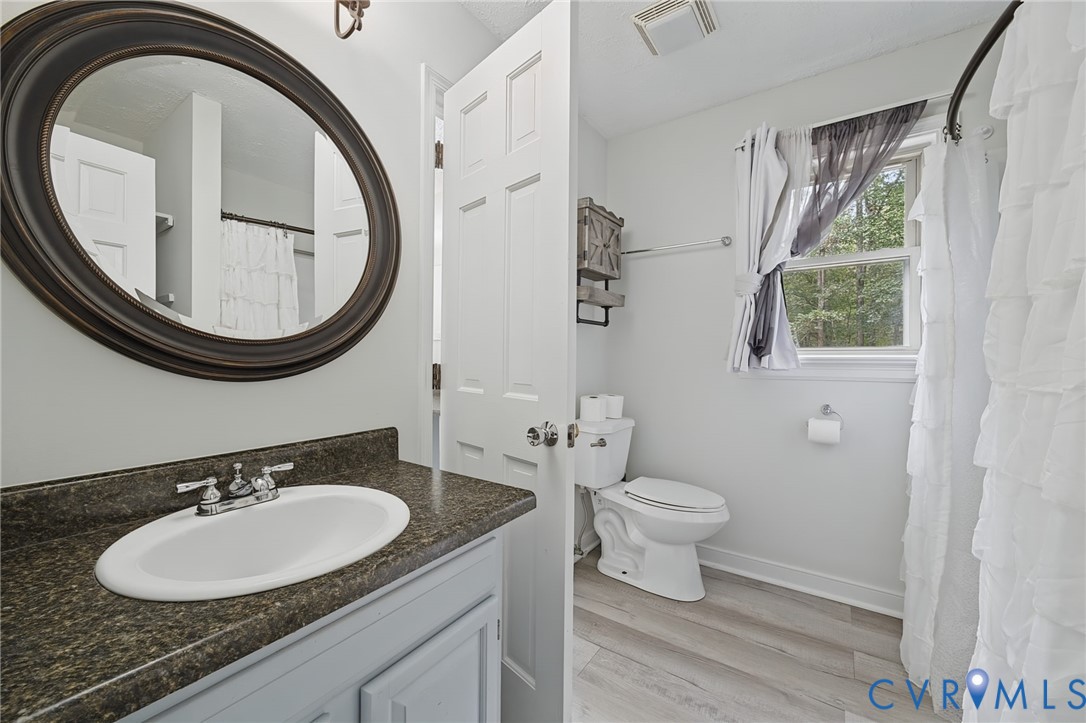 Bathroom featuring a vanity with a dark-toned countertop, integrated oval basin, oval wall-mounted mirror, and wood-finish flooring