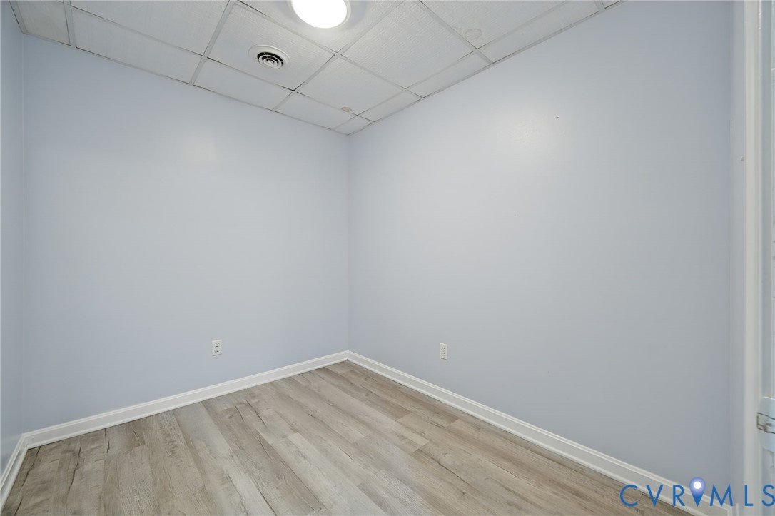 Interior room featuring wood-finish flooring, light-toned walls, and a drop ceiling with a flush-mount light fixture