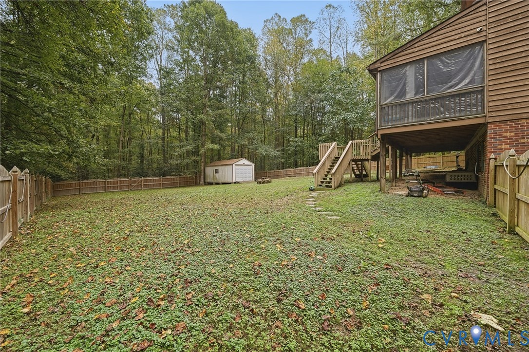 Expansive backyard featuring a wood privacy fence, a detached storage shed, a raised deck with stairs, and a screened porch